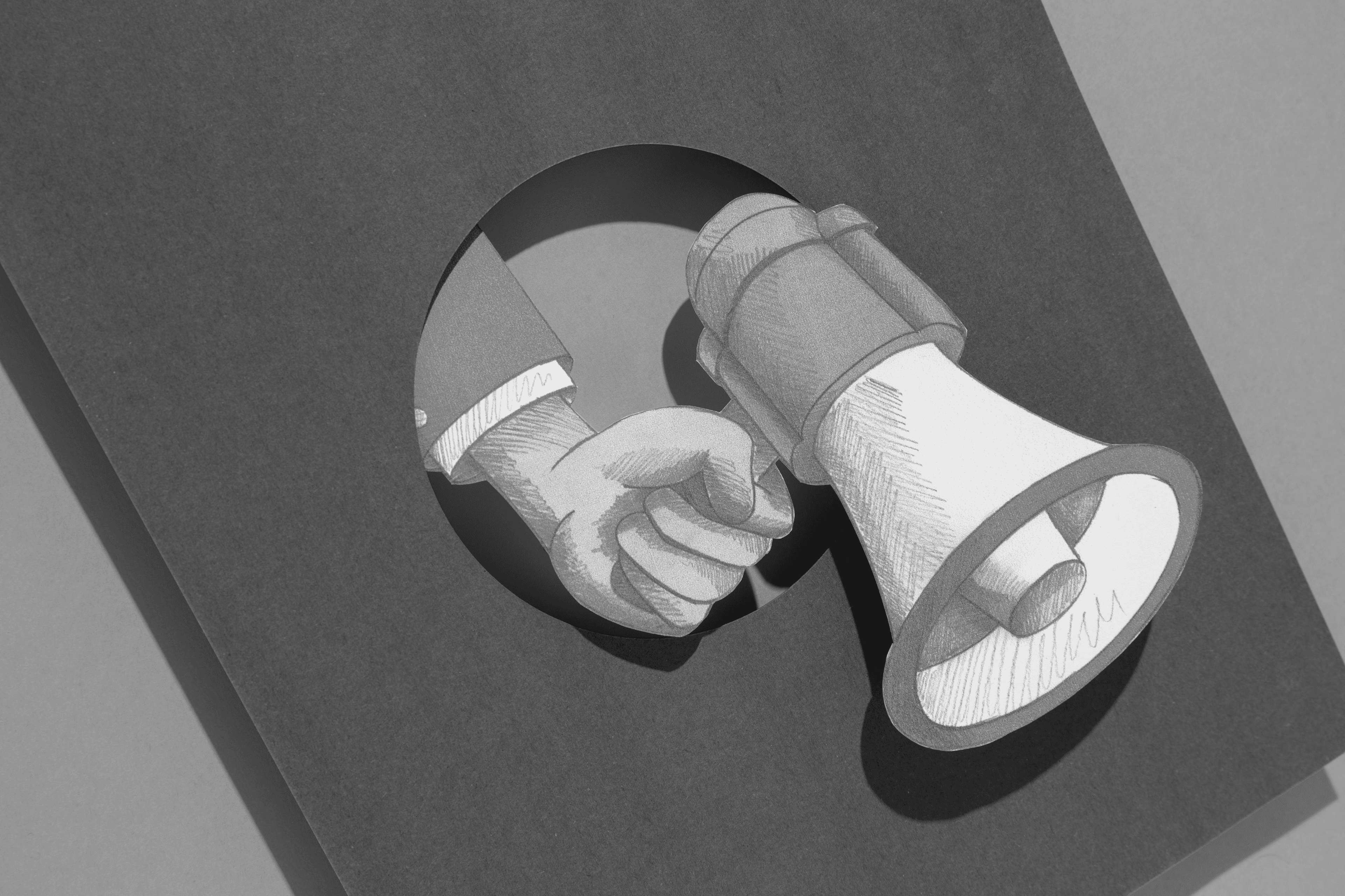 Hand holding a megaphone through a circular cutout